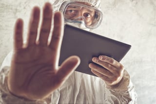 Man in coveralls with clipboard holding up hand warning.